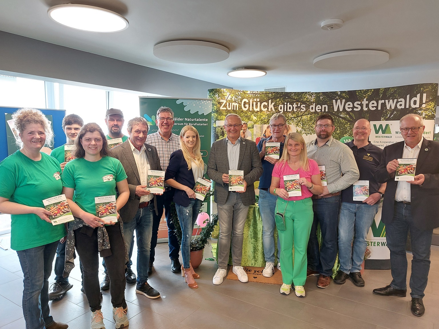 Frauen und Männer stehen mit einer Broschüre in der Hand vor einer Plakatwand.