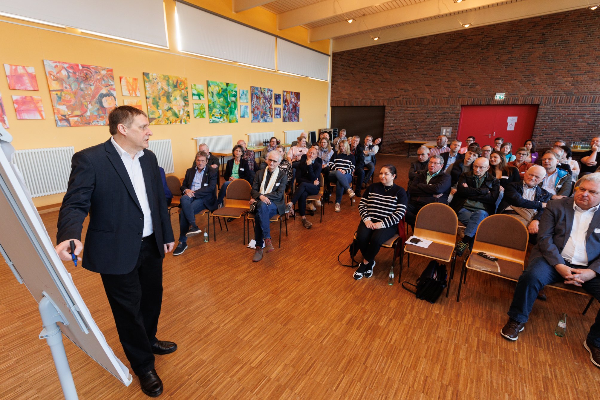Der Referent steht an einem Flipchart. Im Hintergrund sind die gut gefüllten Zuschauerplätze erkennbar.