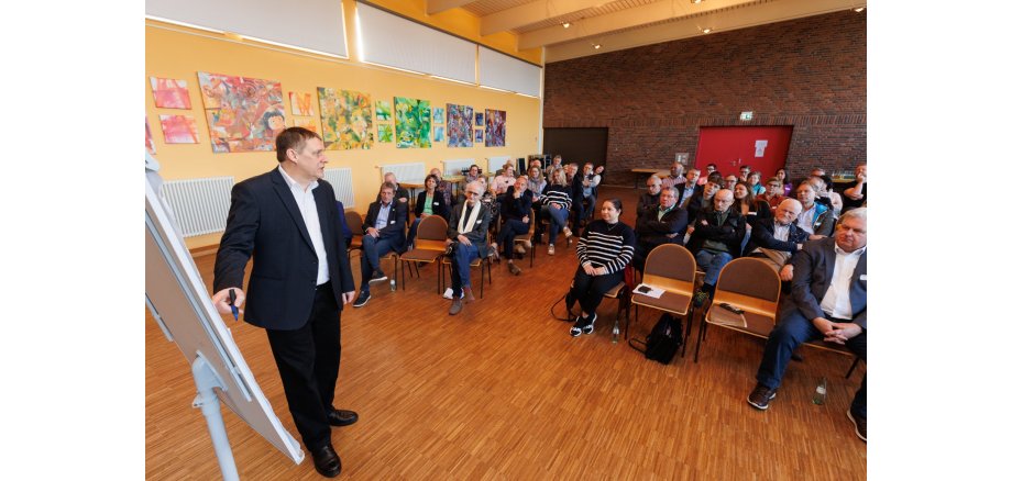 Der Referent steht an einem Flipchart. Im Hintergrund sind die gut gefüllten Zuschauerplätze erkennbar.