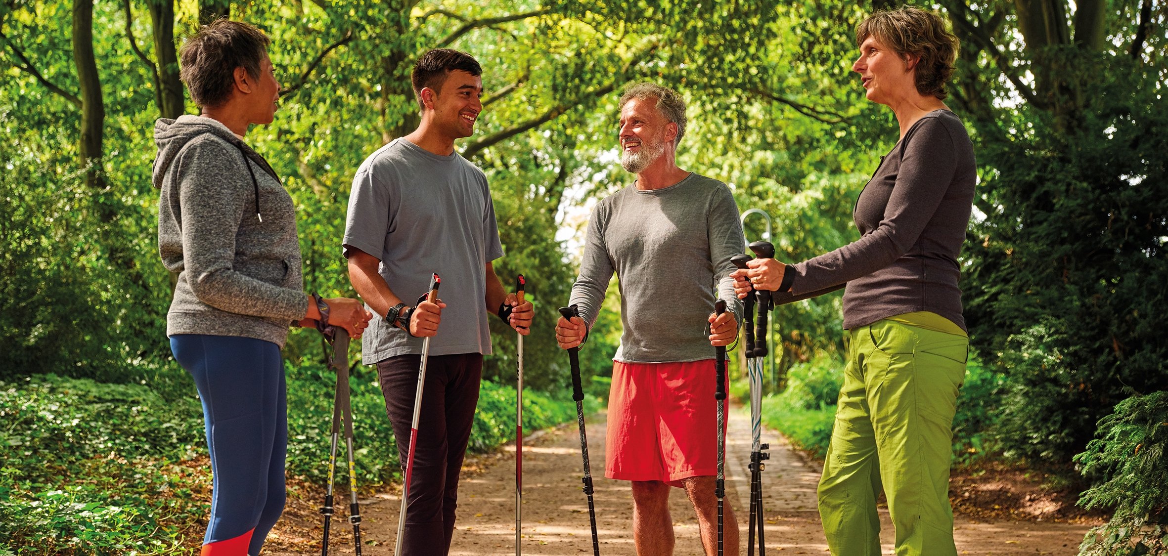Zwei Frauen und zwei Männer mittleren Alters stehen mit Nordic Walking Stöcken in der Hand auf einem Waldweg.
