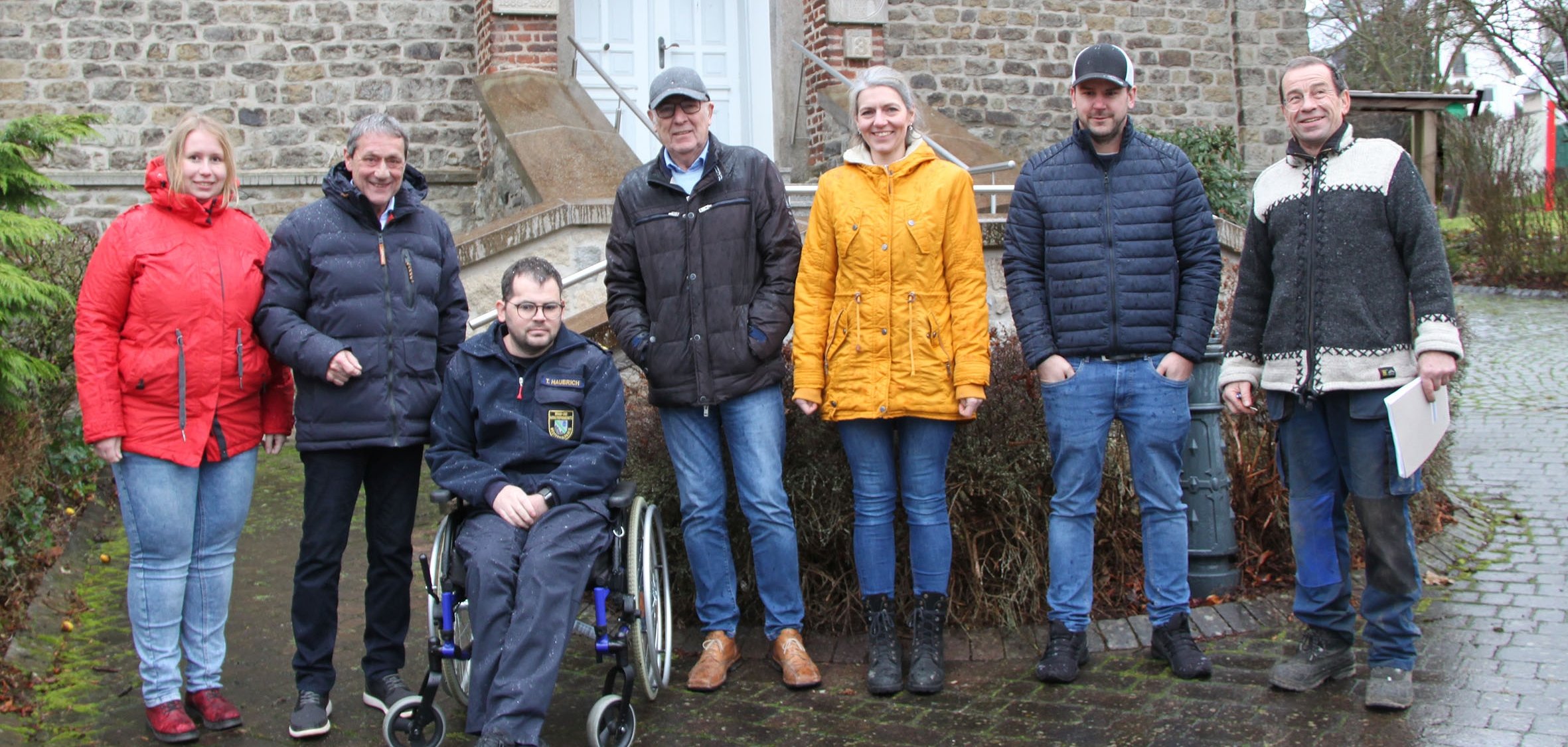 Eine Gruppe von sieben Personen steht im Regen vor der alten Dorfschule in Deesen.