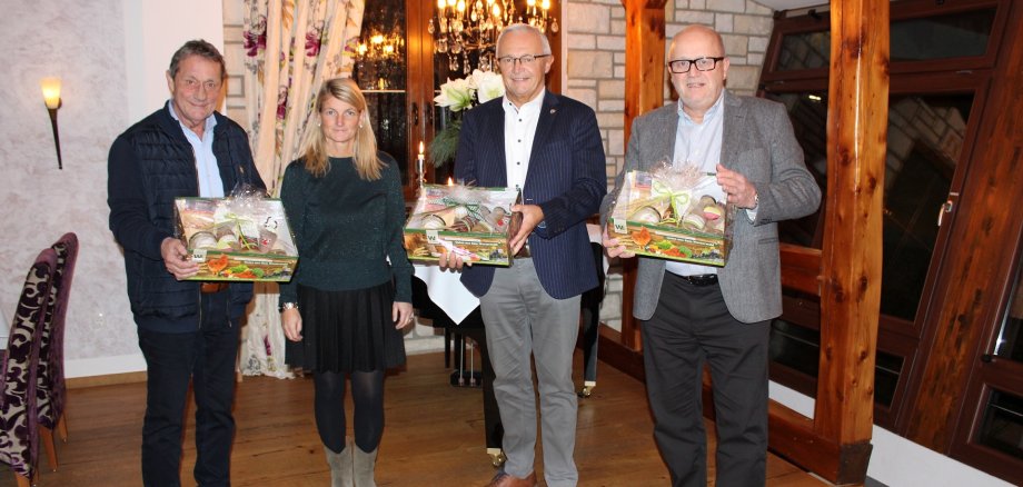 Drei Männer sowie eine Frau stehen mit Geschenkboxen in einem Raum.