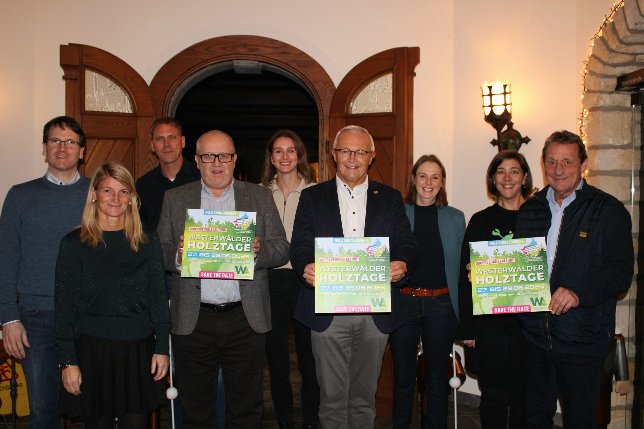 Eine Gruppe Frauen und Männer steht mit Plakaten der Westerwälder Holztage in der Hand in einem Raum nebeneinander.