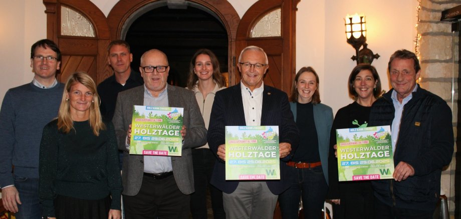 Eine Gruppe Frauen und Männer steht mit Plakaten der Westerwälder Holztage in der Hand in einem Raum nebeneinander.