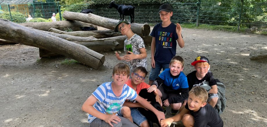 Eine Gruppe von sieben Jungen haben sich vor einem Baumstamm auf einem Spielplatz trapiert. 