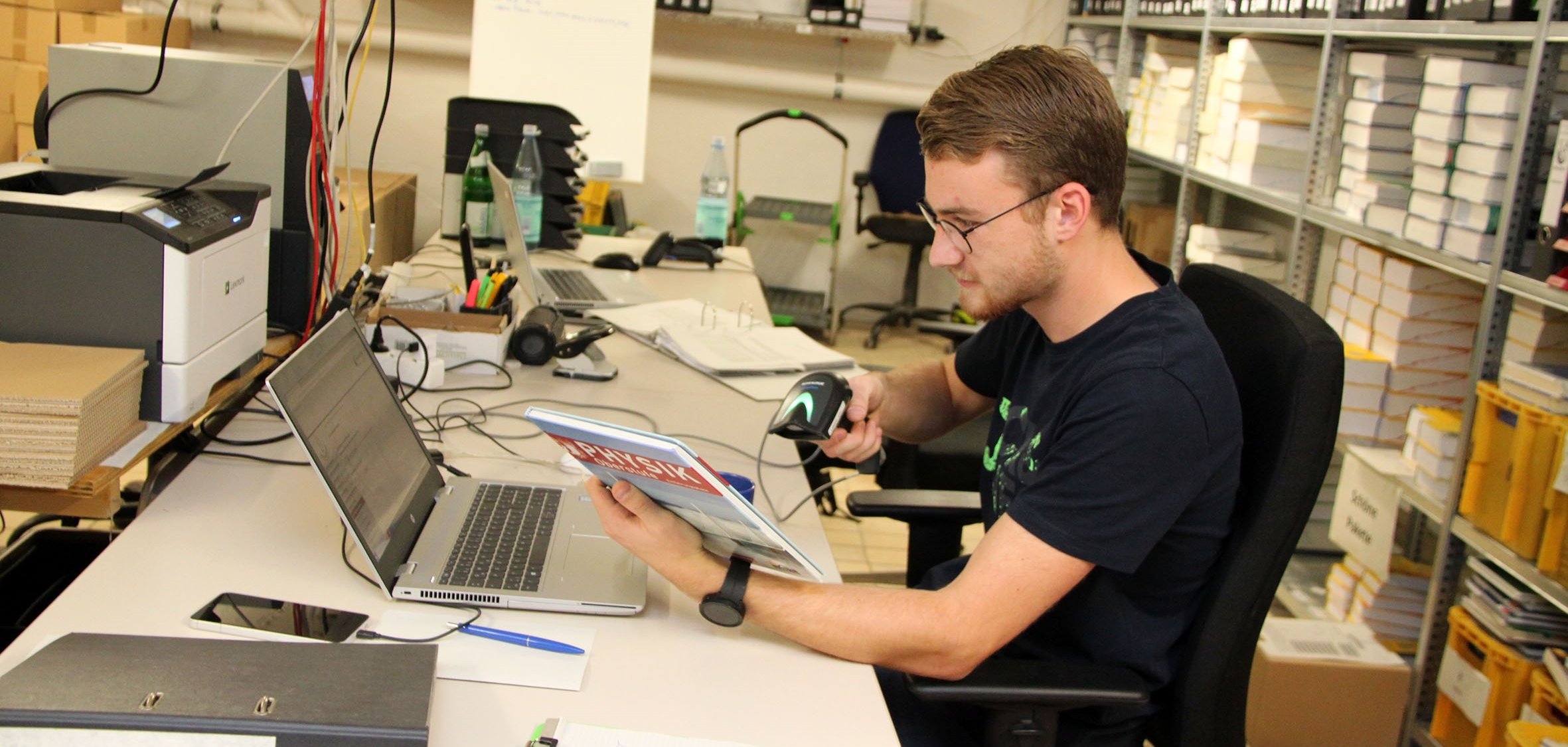 Ein junger Mann scannt den Strichcode eines Schulbuches mit einem Handscanner, um das Buch so im System der Schulbuchausleihe zu registrieren. 