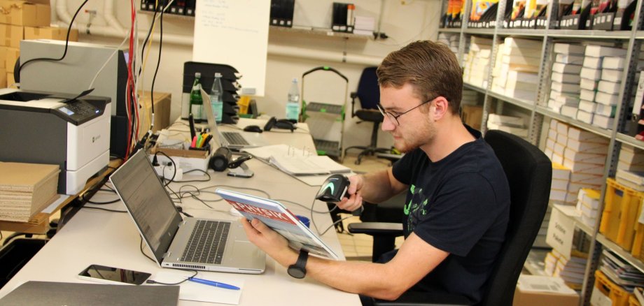 Ein junger Mann scannt den Strichcode eines Schulbuches mit einem Handscanner, um das Buch so im System der Schulbuchausleihe zu registrieren. 