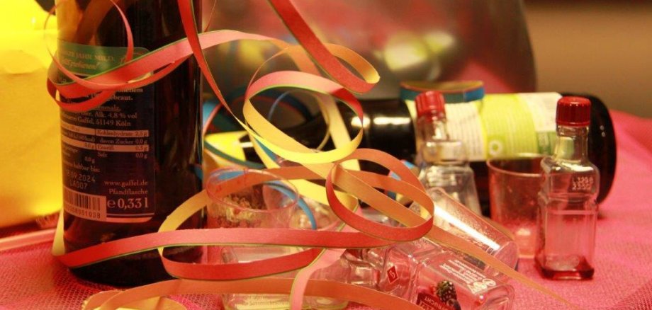Leere Bierflaschen, Schnapsgläschen und -fläschchen, die auf einem, mit Luftschlagen  geschmückten Tisch liegen.