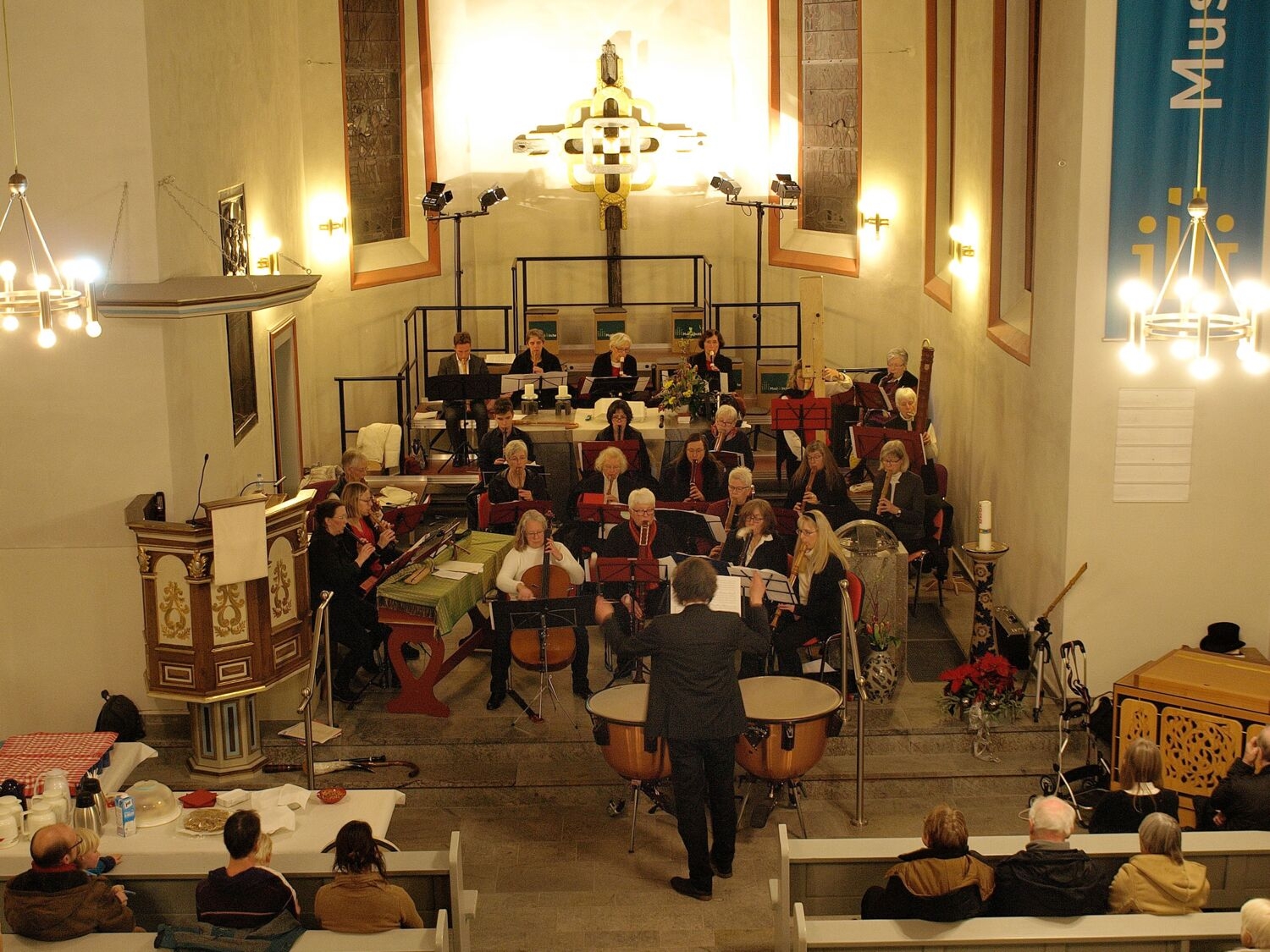 In vorderen Bereich einer Kirche sind zahlreiche Personen aufgereiht, die gemeinsam ihre Streichinstrumente spielen und ein Konzert geben. 