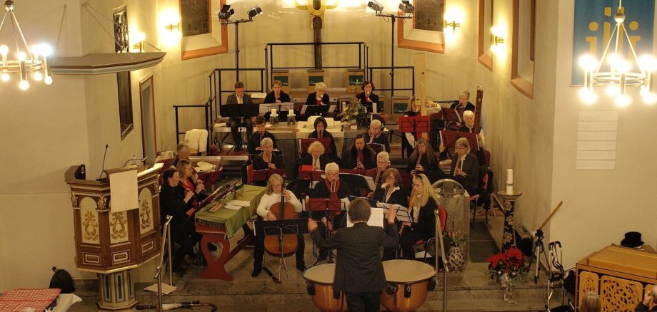 In vorderen Bereich einer Kirche sind zahlreiche Personen aufgereiht, die gemeinsam ihre Streichinstrumente spielen und ein Konzert geben.