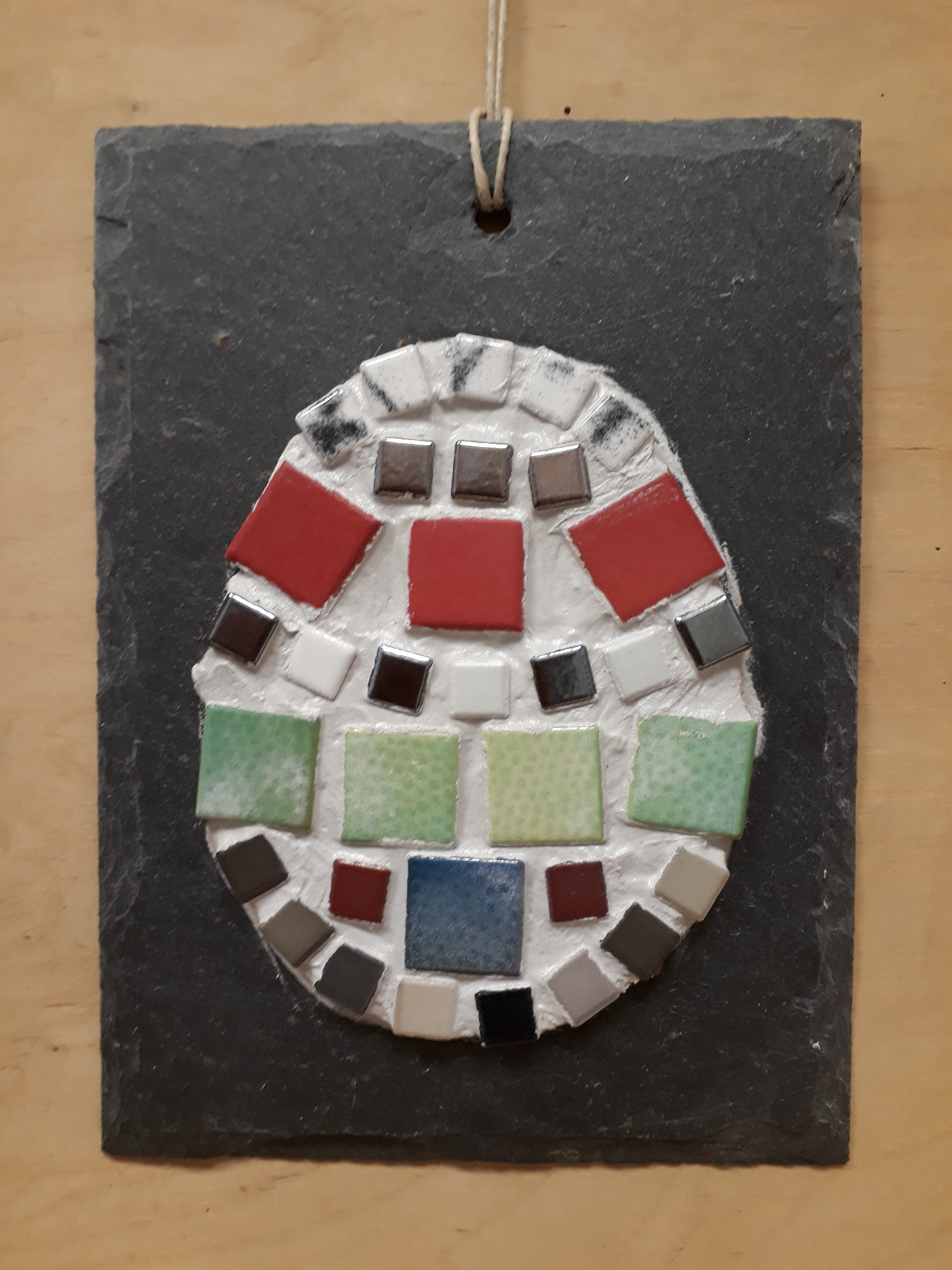 Ein buntes Mosaik-Ei auf einer grauen Schieferplatte.