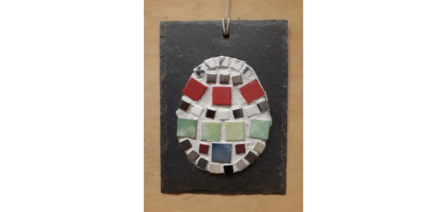 Ein buntes Mosaik-Ei auf einer grauen Schieferplatte.