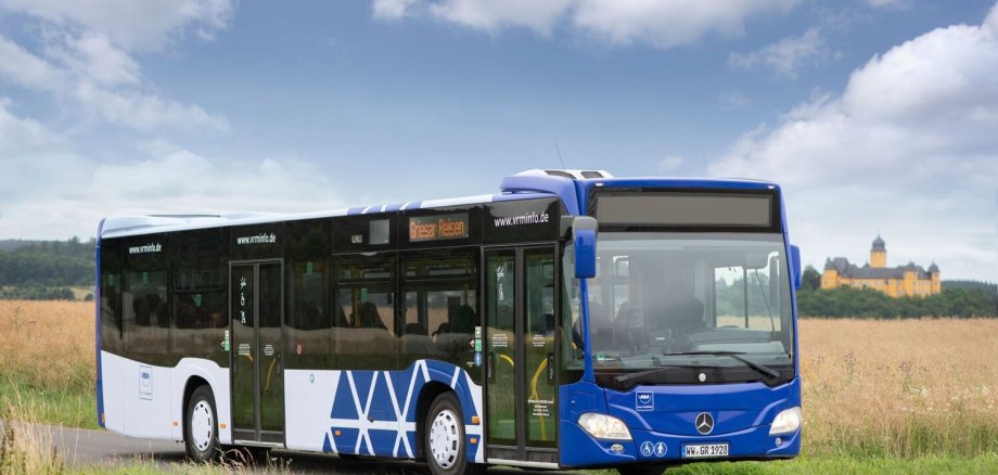 Ein Bus steht vor einem Feld. Im Hintergrund ist das Schloss Montabaur zu sehen.
