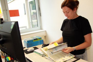Eine Frau blättert vor ihrem Schreibtisch stehend in einem Schulbuch.