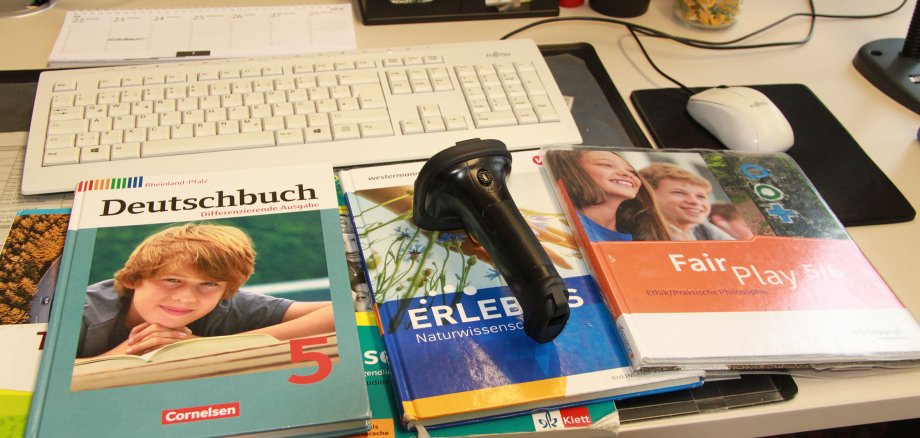 Schulbücher liegen auf einem Büroschreibtisch - oben drauf ein Handscanner.
