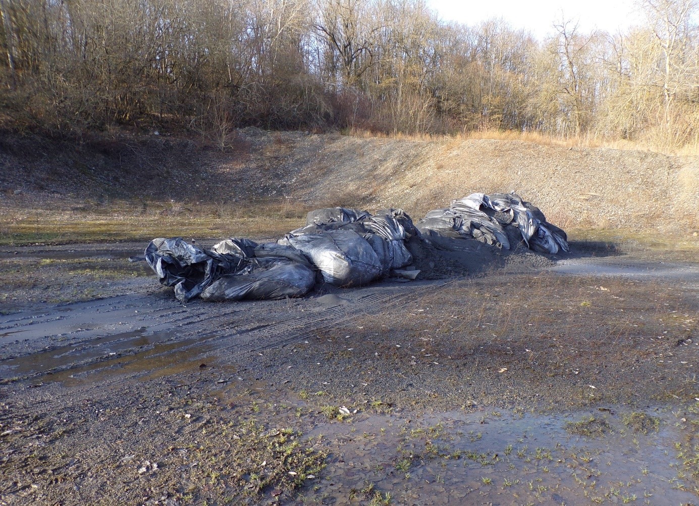 Große schwarze Tüten liegen auf einem Schotterplatz.
