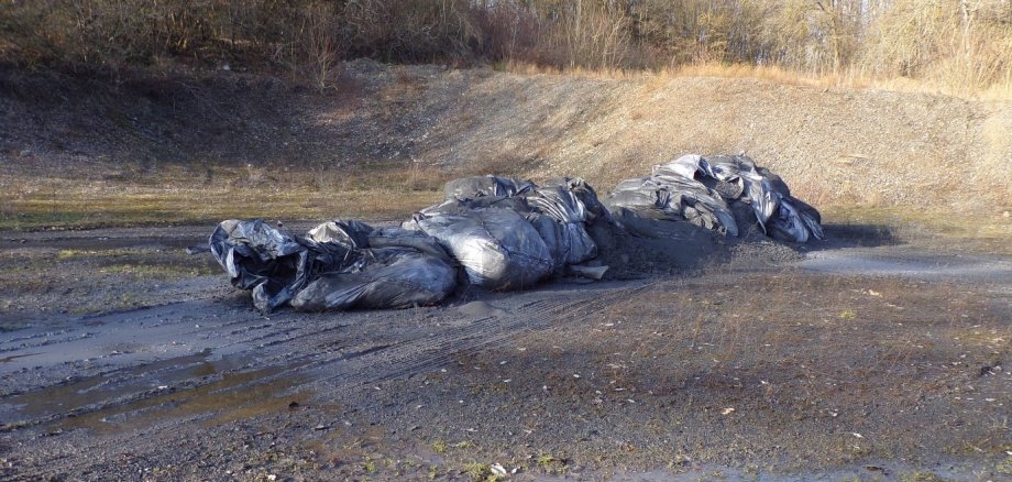 Große schwarze Tüten liegen auf einem Schotterplatz.