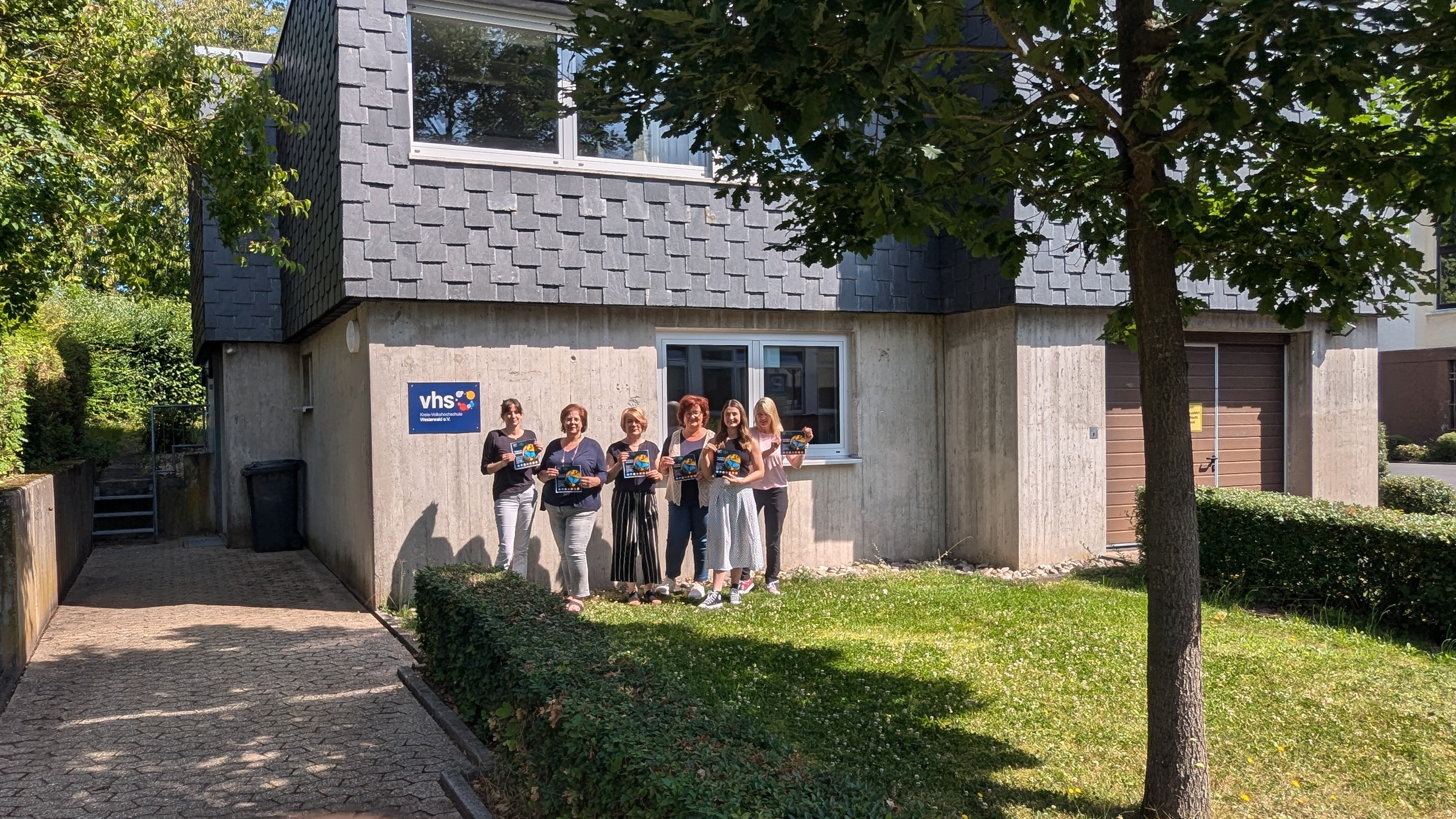 Eine Gruppe steht im Sonnenschein vor einem Gebäude.