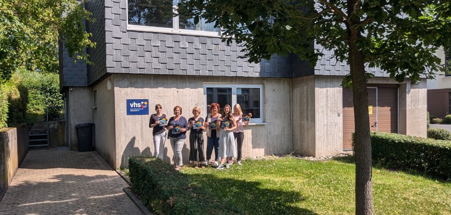Eine Gruppe steht im Sonnenschein vor einem Gebäude.