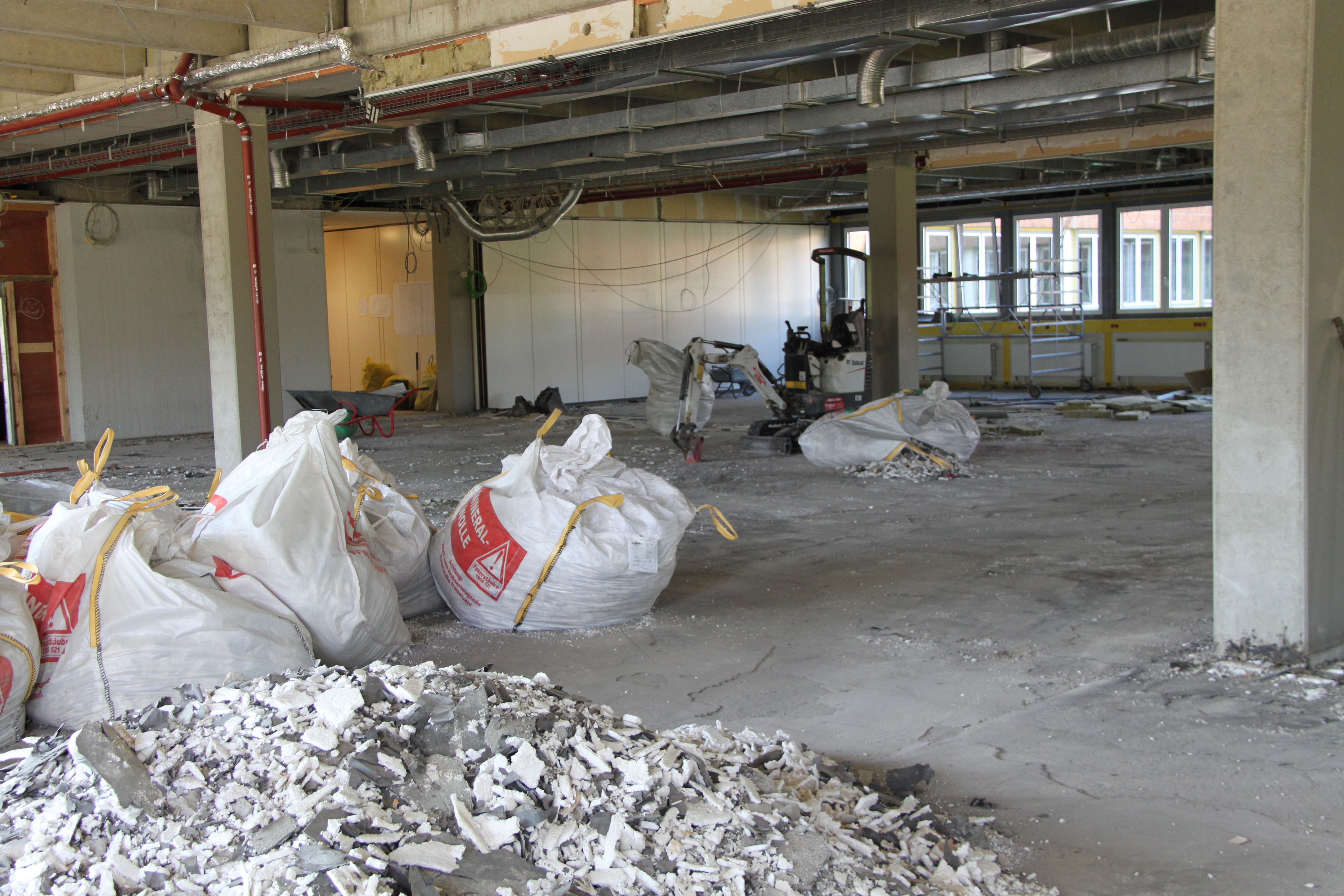 Große weiße Säcke liegen innerhalb eines Raumes mit Säulen, der eine einzige Baustelle ist.