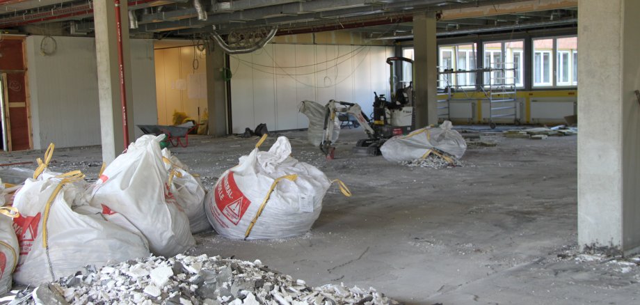Große weiße Säcke liegen innerhalb eines Raumes mit Säulen, der eine einzige Baustelle ist.