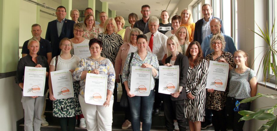Die Institutionen mit einem Teil ihrer Mitarbeitenden stehen im Foyer der Kreisverwaltung Montabaur und halten die Zertifikate in die Kamera.