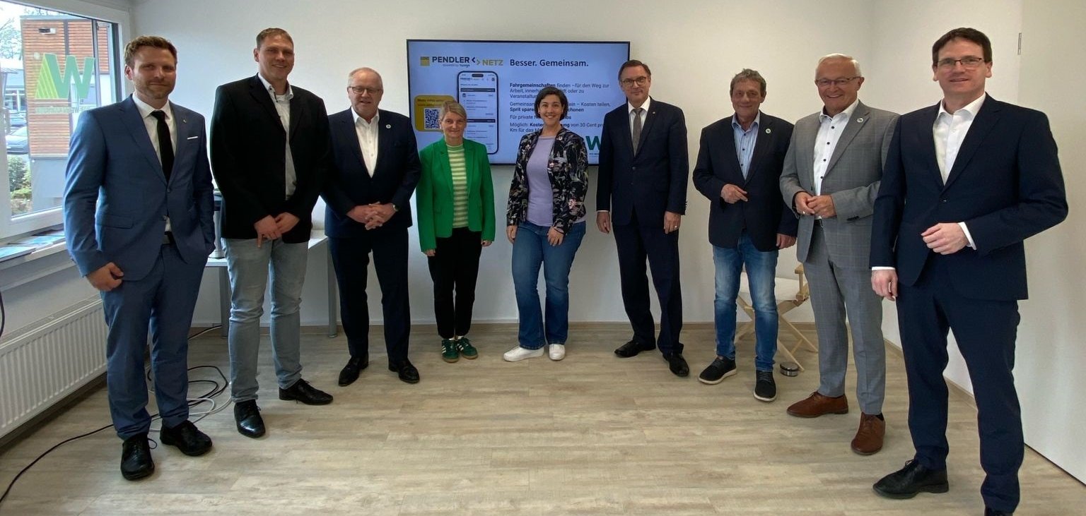 Personen stehen in einem Raum vor einer digitalen Tafel und lächeln freundlich in die Kamera