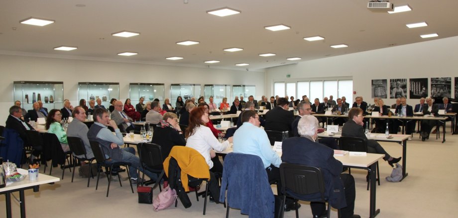 Eine große Gruppe Menschen sitzt an in U-Form aufgestellten Tischen.