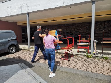 Ein Mann und eine Frau tragen Stühle in ein Gebäude.