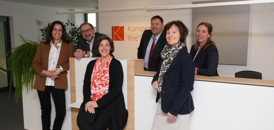 Sechs Personen stehen in einer Räumlichkeit und schauen freundlich in die Kamera
