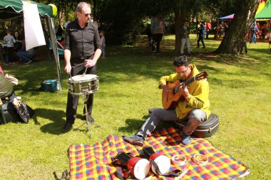 Auf einer bunten Picknickdecke im Grünen musizieren zwei Männer. 