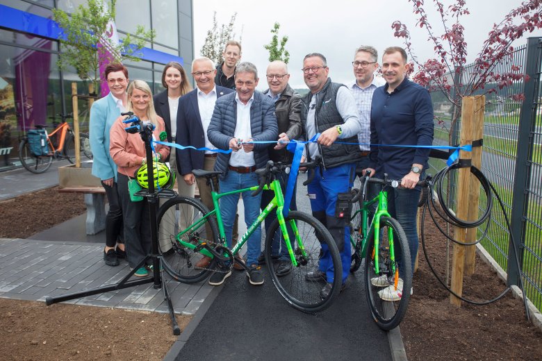 Die Gruppe steht vor einem Fahrradgeschäft und Landrat Achim Schwickert in der Mitte. Mit einer Schere durchschneidet er ein blaues Band, darunter stehen die beiden grünen Bikes.
