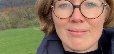 Eine junge Frau mit Brille steht auf einer Wiese.