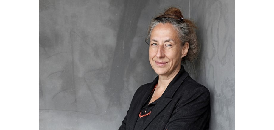 Porträtfoto einer Frau mit hochgesteckten Haaren in einem schwarzen Blazer.