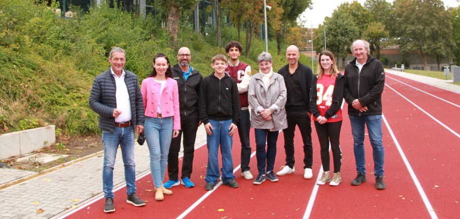 Eine Gruppe von Menschen steht auf einer roten Laufbahn. Im Hintergrund ist das Hallendach des Außensportbereiches zu sehen.