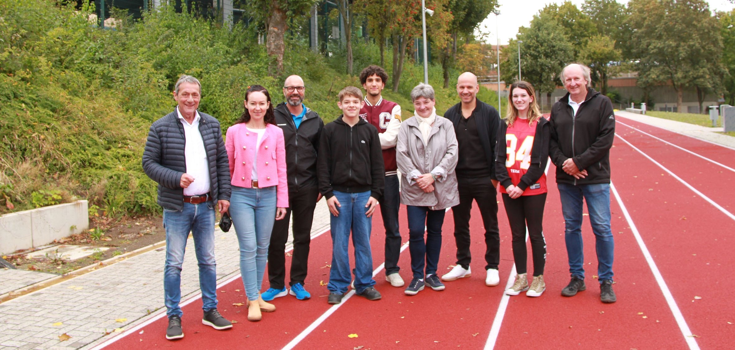 Eine Gruppe von Menschen steht auf einer roten Laufbahn. Im Hintergrund ist das Hallendach des Außensportbereiches zu sehen.