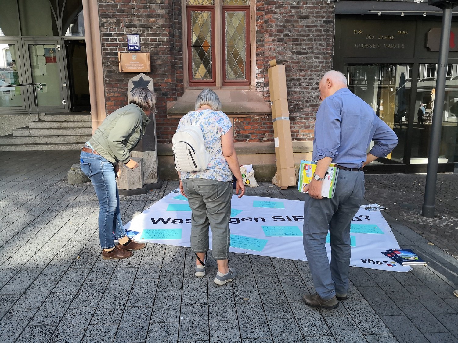 Drei Menschen betrachten ein auf dem Boden liegendes Plakat.