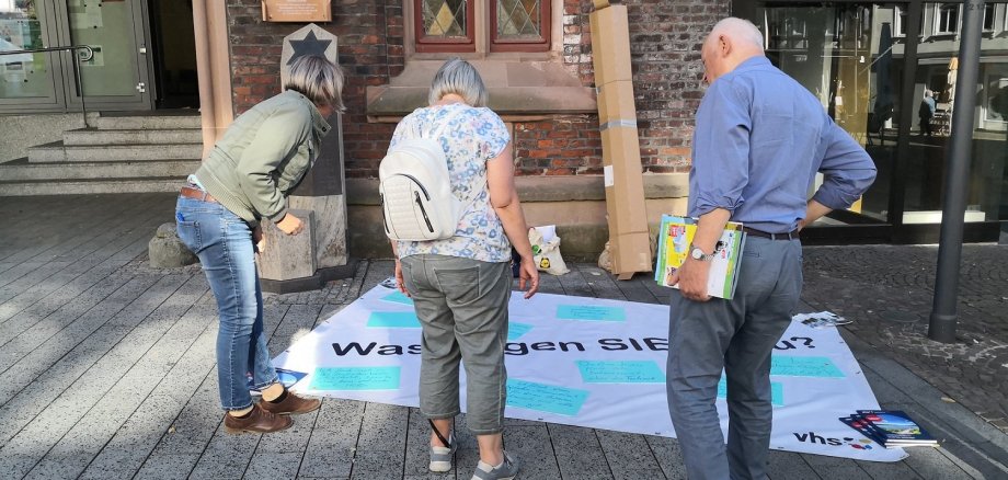 Drei Menschen betrachten ein auf dem Boden liegendes Plakat.