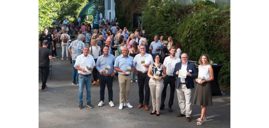 Menschen stehen vor der Westerwald-Brauerei und unterhalten sich, im Vordergrund hält unter anderem Landrat Achim Schwickert einen Flyer in die Kamera.