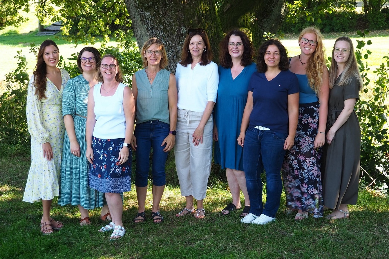 Eine Gruppe Frauen steht freundlich lächelnd vor einem Baum in einem Park.