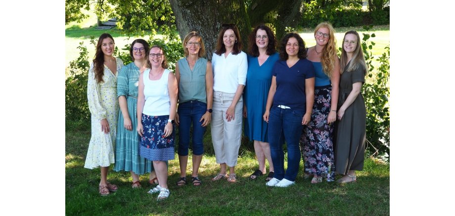 Eine Gruppe Frauen steht freundlich lächelnd vor einem Baum in einem Park.