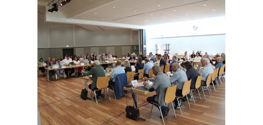 Männer und Frauen sitzen in einer inneren und einer äußern U-Formation im Bürgerhaus.