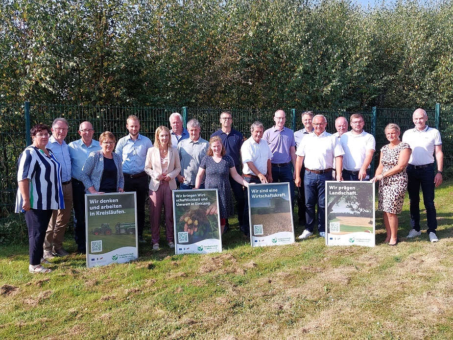 Eine Gruppe von Frauen und Männern steht mit Plakaten auf einer Wiese.