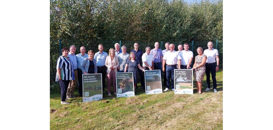 Eine Gruppe von Frauen und Männern steht mit Plakaten auf einer Wiese.