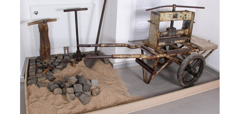 Ein altes Gerät zum Steinbrechen und bearbeitete Pflastersteine sind in der Museumsausstellung.