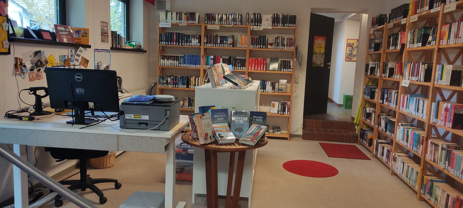 In einer Bibliothek stehen mit Büchern gefüllte Regale und ein Schreibtisch.