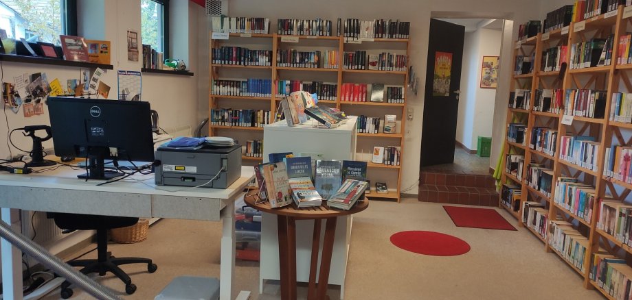 In einer Bibliothek stehen mit Büchern gefüllte Regale und ein Schreibtisch.