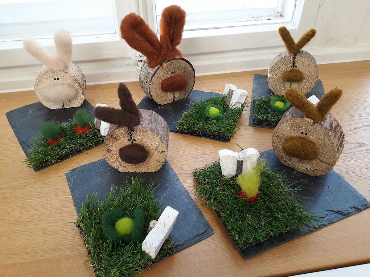 Auf Schieferplatten stehen Baumstammscheiben, die als Hasen verziert sind.