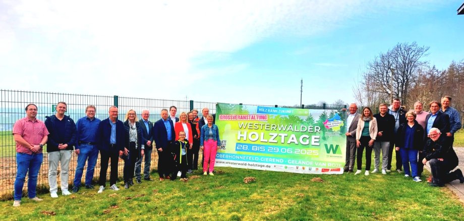 Auf einer Wiese steht eine Gruppe Frauen und Männer neben einem Banner, das für die Westerwälder Holztage wirbt.