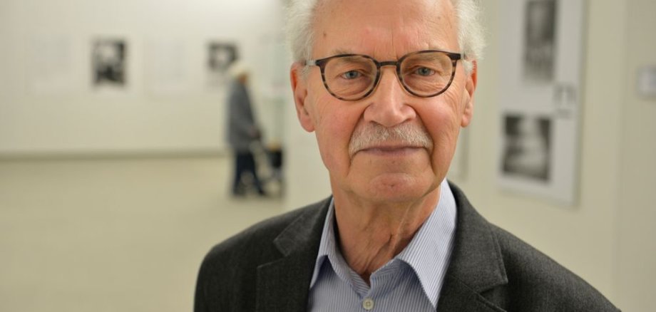 Ein Herr mit weißen Haaren und Brille schaut in die Kamera.